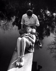 a man sitting on the edge of a body of water next to a woman