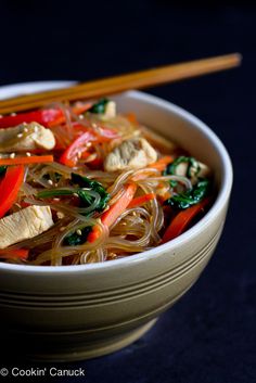 a bowl filled with noodles and vegetables next to chopsticks on a black surface