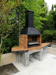 an outdoor brick pizza oven in the middle of a patio with trees and bushes behind it