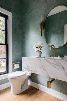 a white toilet sitting next to a bathroom sink under a round mirror in a green room