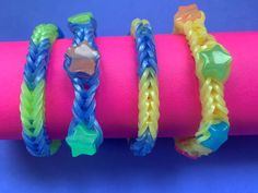 three different colored bracelets on top of a pink tube with blue and yellow braiding