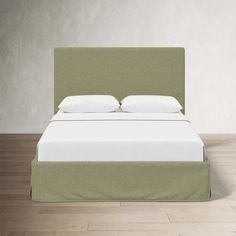 a bed with white pillows and green headboard on hardwood flooring in an empty room