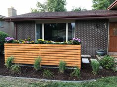 a wooden planter in front of a brick house with flowers growing on the windowsill