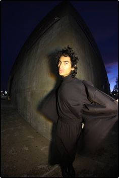 a man standing in front of a building at night with his coat over his shoulders