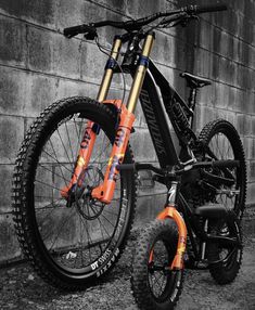 an orange and black bike parked next to a brick wall