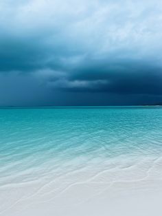 the sky is dark and cloudy over the water at this beach area with white sand