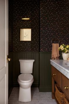 a white toilet sitting inside of a bathroom next to a sink and wooden cabinetry