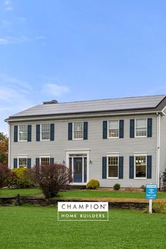 a large white house with blue shutters and a sign for champion homes in front of it