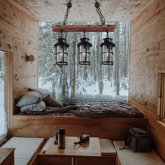 a bed sitting inside of a wooden cabin next to a window filled with snow covered trees