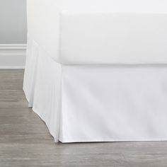 a bed with white sheets on top of it and wood flooring in the background