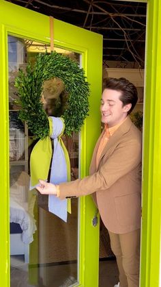 a man standing in front of a green door with a wreath on top of it