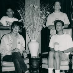 black and white photograph of four men sitting in chairs with vases on the floor