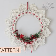 a crocheted christmas wreath hanging on the wall with red berries and pine cones