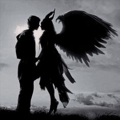 a man and woman standing next to each other in front of the sky with large wings