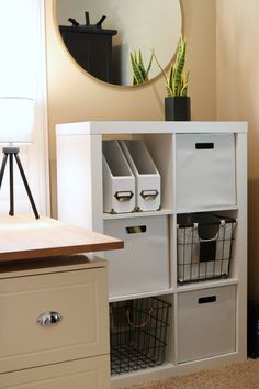 a white shelf with baskets and bins in front of a mirror on the wall