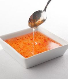 a spoon pouring sauce into a square white bowl