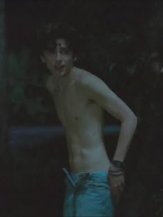 a shirtless young man standing in the woods at night with his hands on his hips