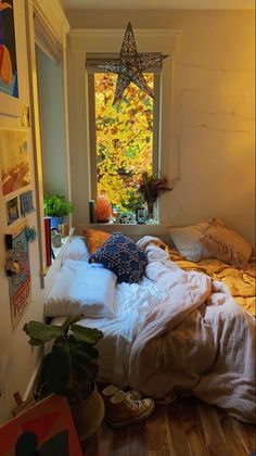 an unmade bed sitting in front of a window next to a potted plant