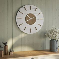 a white clock sitting on top of a wooden shelf next to a vase with flowers