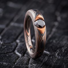 "* Price may vary depending on ring size, please inquire with us directly with your needed size for accurate pricing! This dark and moody mokume gane ring evokes the feeling of an enchanted forest.  This cathedral style ring features a shiny black diamond, a low dome profile, and an etched and oxidized finish, which paired with the Woodgrain pattern creates the look of smoldering wood. The Embers palette features Red Gold, Palladium and Sterling Silver.  *Price does NOT include stones or setting fees* Pattern: Woodgrain  Palette: Embers Finish: Etched & Oxidized Profile: Low Dome Width Shown: 5-3mm Tapered Width Size Shown: 6.5 Stone: 5mm Black Diamond Setting Style: Cathedral We care about customer service and would like to hear from you! Please contact us to help create your treasured it Gloom Wedding Ring, Obsidian Engagement Ring Men, Obsidian Ring Mens, Obsidian Mens Wedding Band, Black Obsidian Ring, Mokume Gane Ring, Cathedral Ring, Mokume Gane, Mens Silver Rings