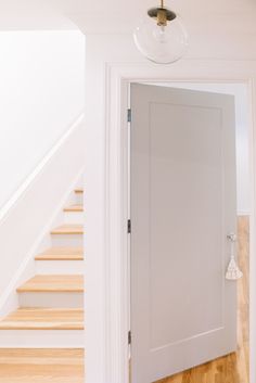 an open door leading to a hallway with wooden floors and white walls, in front of a stair case