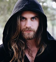 a man with long hair and beard wearing a black hoodie looking at the camera