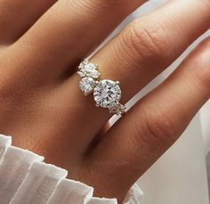 a woman's hand with a diamond ring on top of her finger and the other hand holding an engagement ring