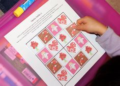 a child's hand holding a piece of paper over a pink box with pictures on it