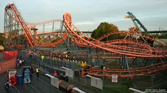 the roller coaster at an amusement park with people walking around and riding on it's side