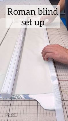 a person is cutting paper with scissors on a table that has the words roman blind set up