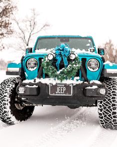 a blue jeep with a wreath on it's hood parked in the snow near trees