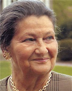 an older woman wearing a necklace and jacket smiling at the camera with grass in the background