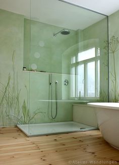 a bathroom with a tub, shower and wooden flooring in front of a window