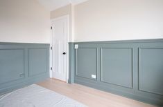 an empty room with wood flooring and green painted paneling on the walls, along with a white door