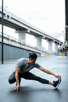 a man stretching out on the ground with his foot in front of him and an overpass behind him