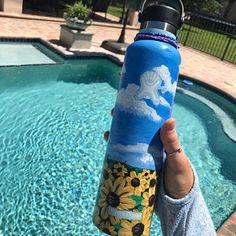 a person holding up a water bottle in front of a swimming pool with sunflowers on it