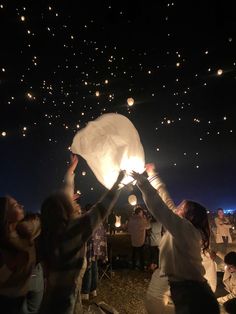 people releasing paper lanterns into the sky at night with stars in the sky behind them