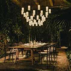 a dining room table with chairs and lights hanging from it's ceiling in the middle of an outdoor area