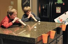 two young boys are playing baseball on the counter top in front of an open refrigerator