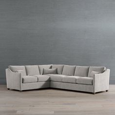 an l - shaped sectional sofa with pillows on the back and sides, in front of a gray wall