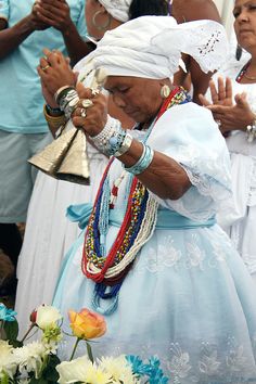 an older woman in blue dress and white headdress standing next to other people