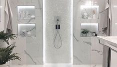 a bathroom with white marble walls and flooring, including a shower head mounted to the wall