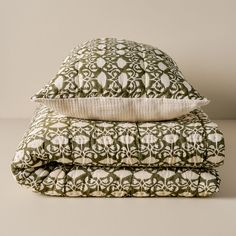 two pillows stacked on top of each other with white and green designs in the middle