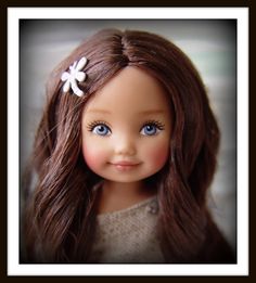 a close up of a doll with long brown hair and blue eyes, wearing a white flower in her hair