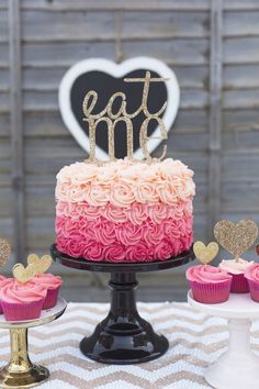 a cake with pink and gold frosting sitting on top of a table next to cupcakes