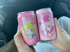 two pink soda cans with sailor and princess images on them in someone's hand