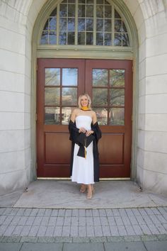 a woman standing in front of a door with her arms wrapped around her shoulders, wearing a white dress and black shawl