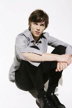 a young man sitting on the ground with his legs crossed, wearing black pants and a gray shirt