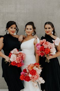 three bridesmaids in black dresses with red and pink flowers on their bouquets