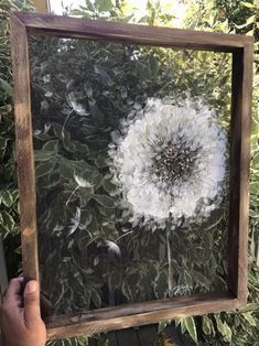 a person holding up a frame with a painting of a dandelion